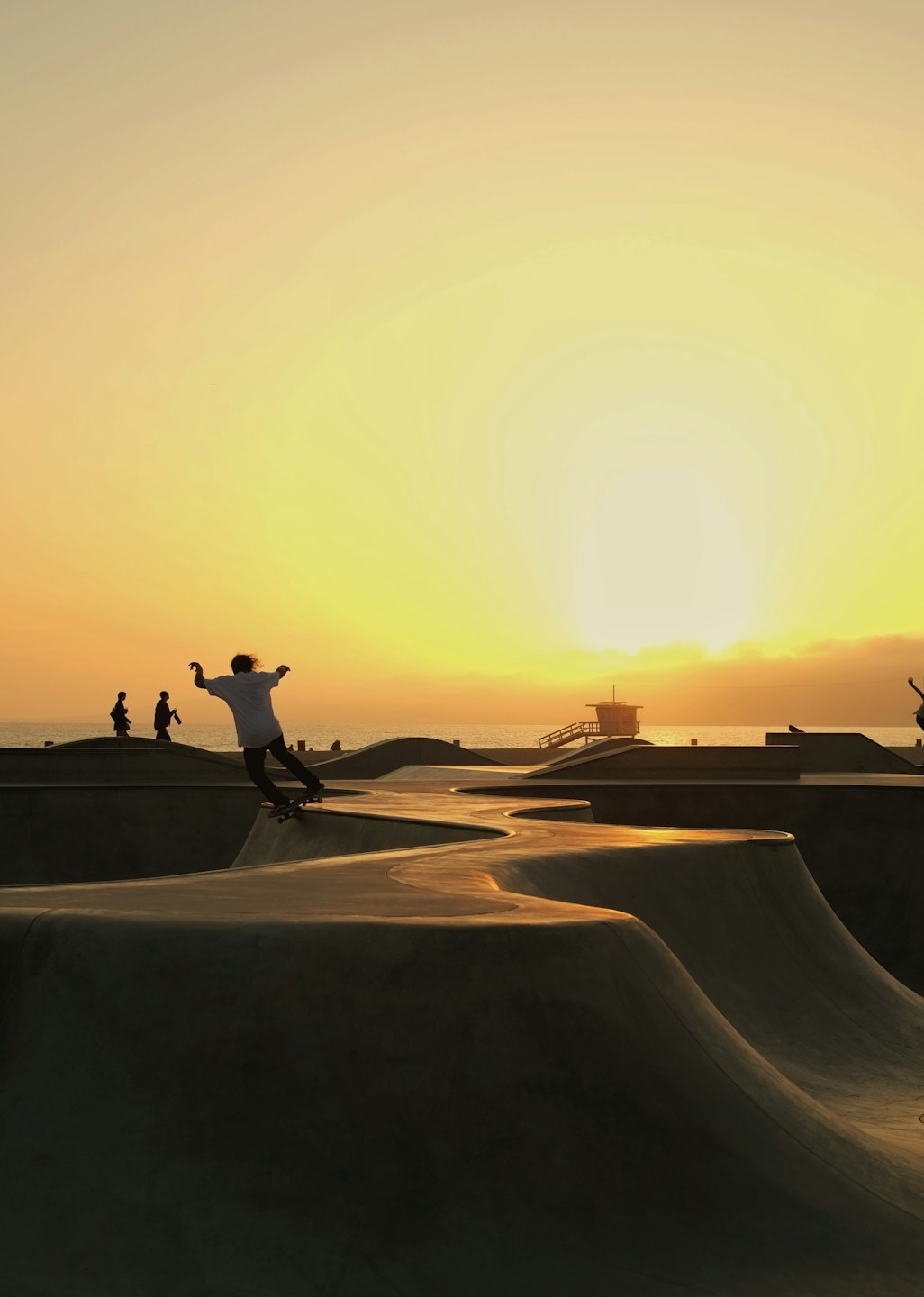 Young person grinds skateboard on concrete ramp at sunset.
