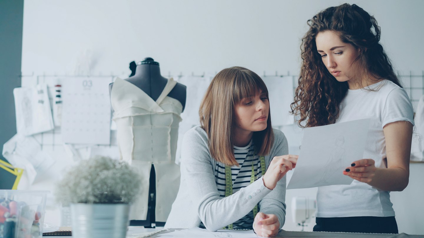 Two fashion designers discuss a sketch in their creative studio.